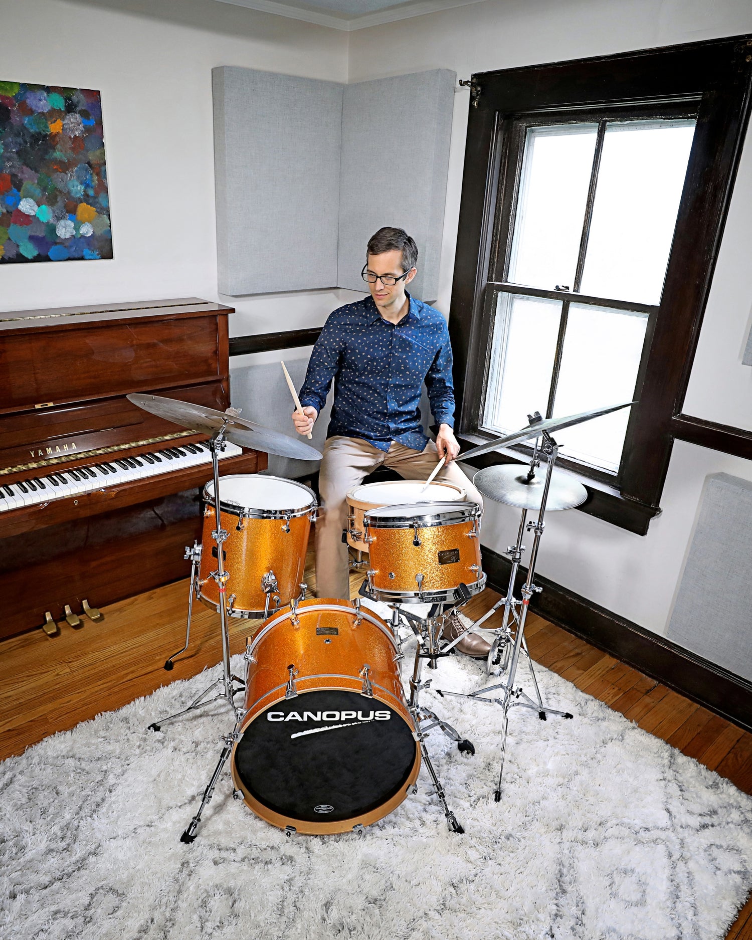 Matt playing drums in a room with a piano and window